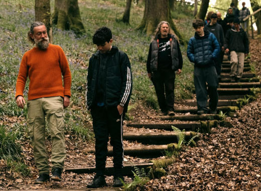 A mentor in an orange jumper walking down woodland steps with a boy, others following behind