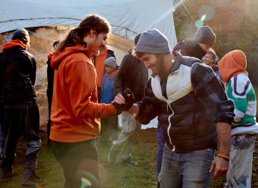 A boy and a man laughing as they shake hands at a gathering in the woods
