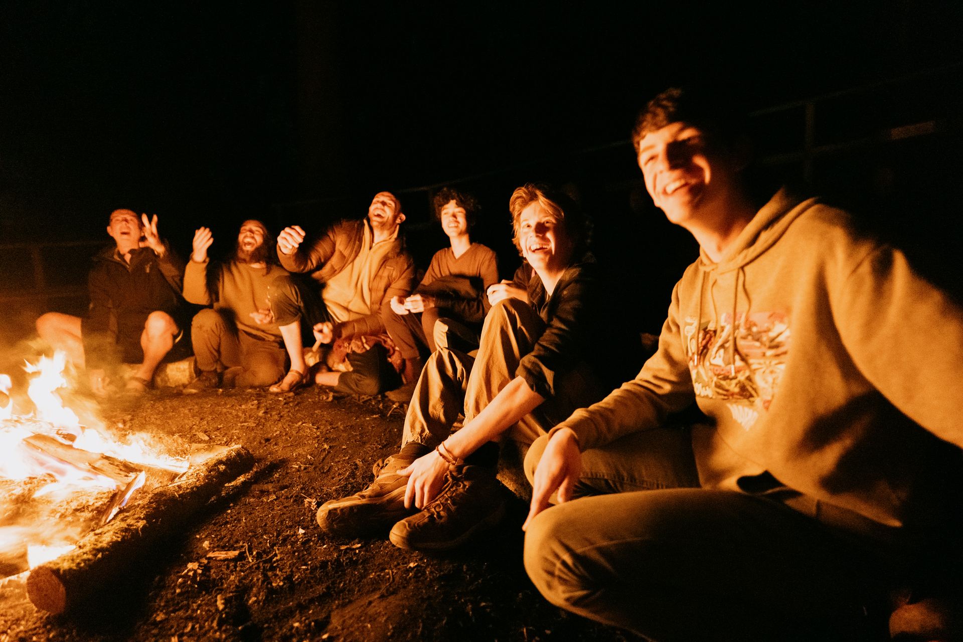 Boys and mentors laughing around the fire at night