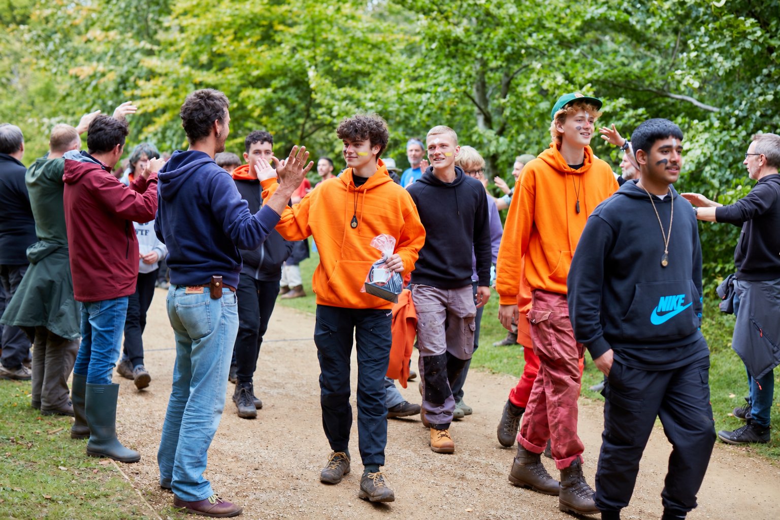 Boys walking down a woodland path through a line of men cheering them on