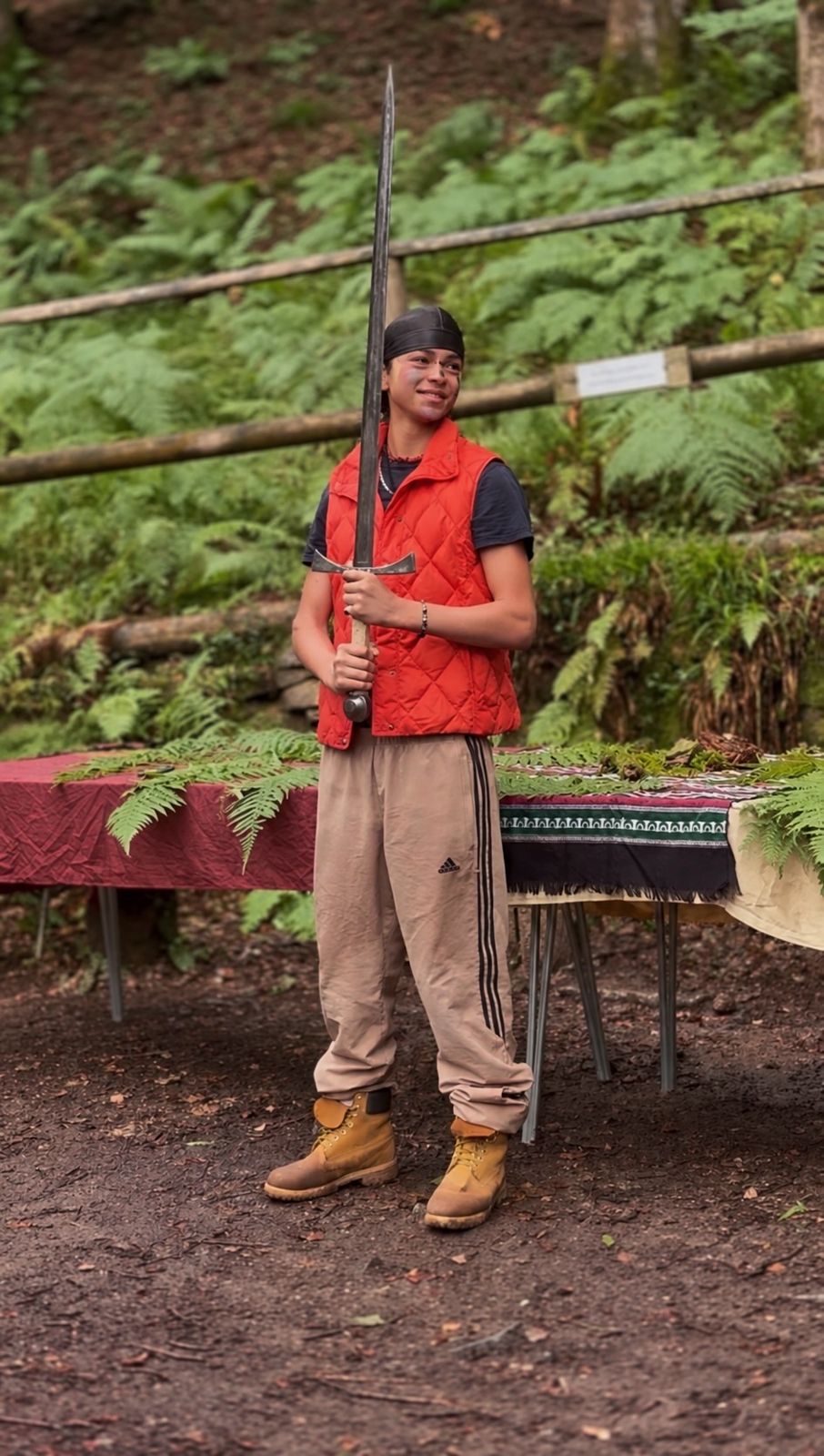 A boy in a red gilet holding a staff in the woods