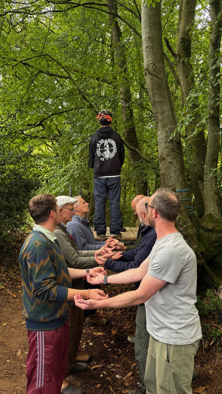 Boys and men joining hands in a line under the trees