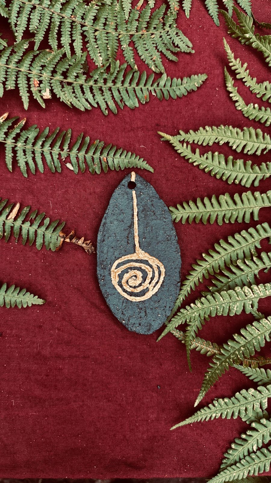A carved pendant laid on ferns and red cloth