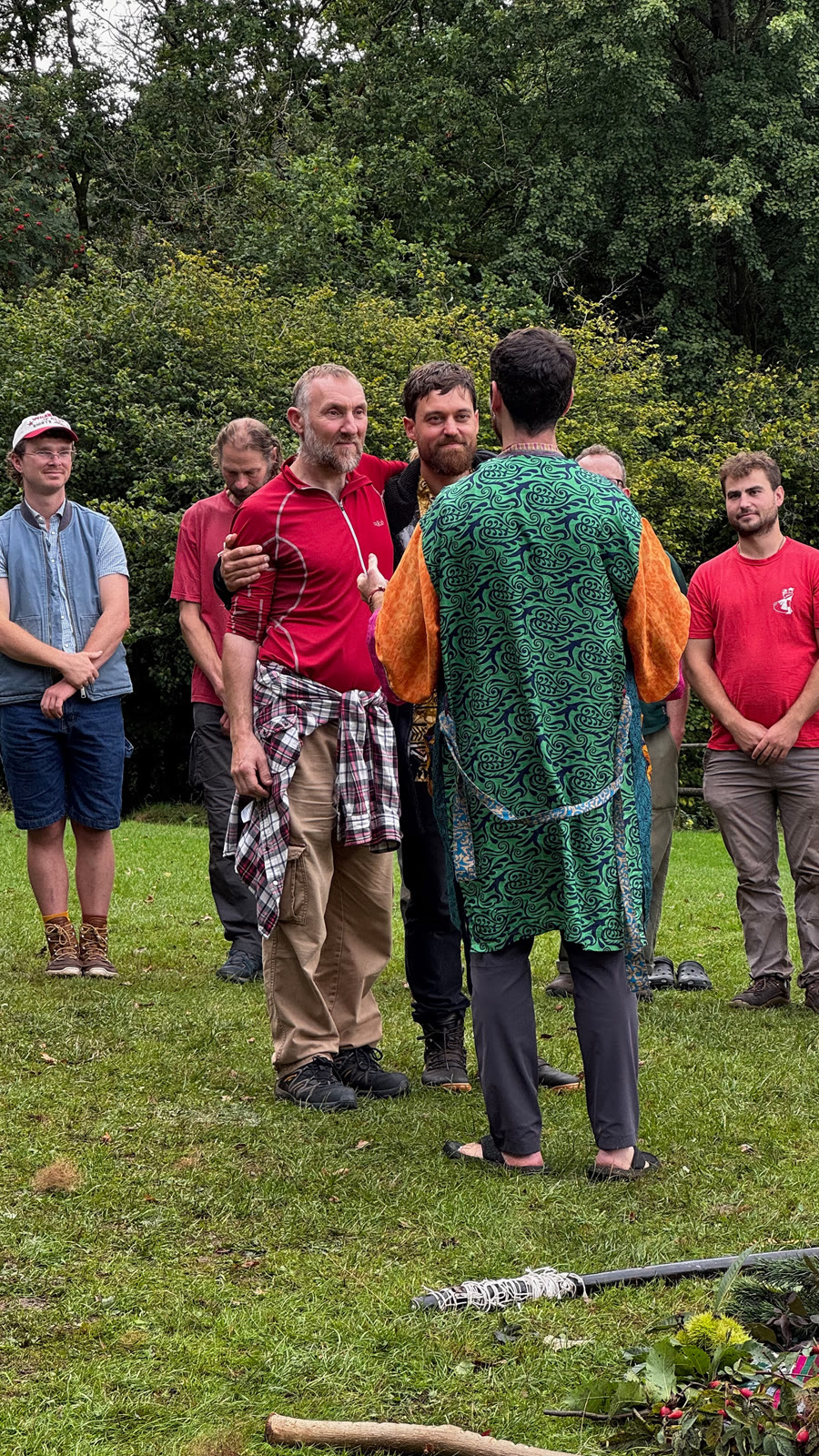 A man in a green robe standing in front of a circle of mentors on the grass